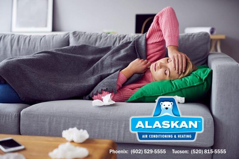 Woman laying on couch under blanket with tissues with Alaskan AC logo and contact info