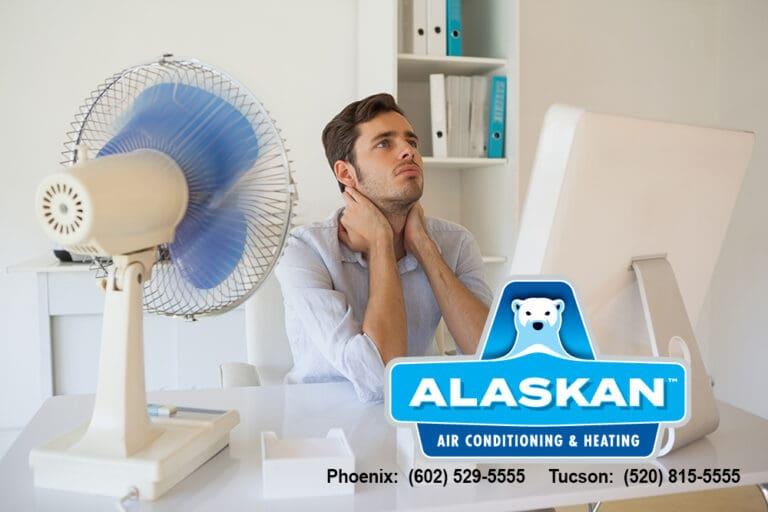 Man sitting at desk with fan blowing on him, looking distressed, with Alaskan AC logo and contact info