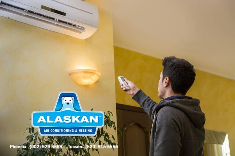 man pointing remote at split system mounted near ceiling with Alaskan AC logo and contact info