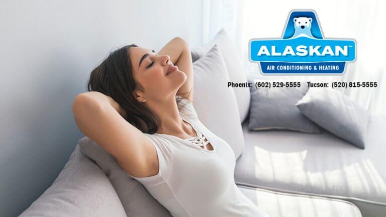 Woman sitting on couch, hands behind head, smiling with eyes closed, Alaskan Air Conditioning and Heating logo and contact phone numbers