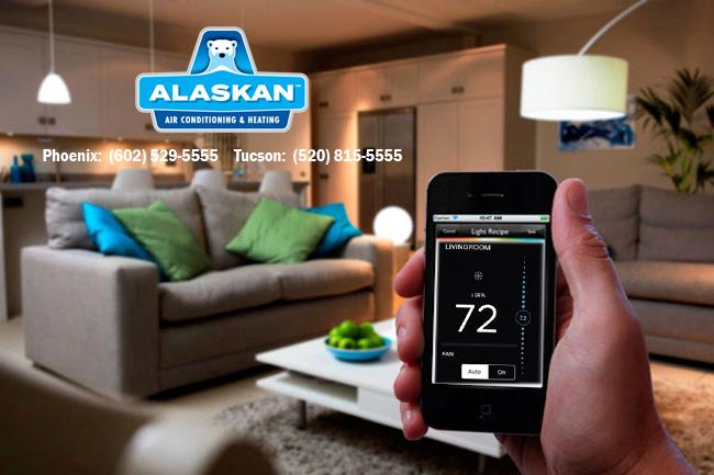 hand holding phone with thermostat app open, living room in background, with Alaskan Air Conditioning and Heating logo and contact phone numbers in upper left quadrant